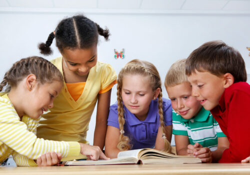 Portrait of pupils looking at page of encyclopaedia at reading lesson